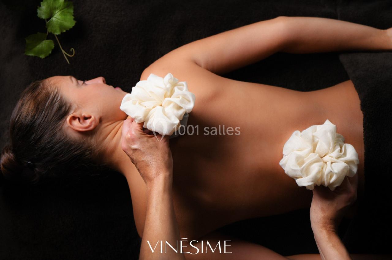 Femme allongée sur le ventre recevant un massage avec des pochons en tissu sur le dos, sur un drap sombre.