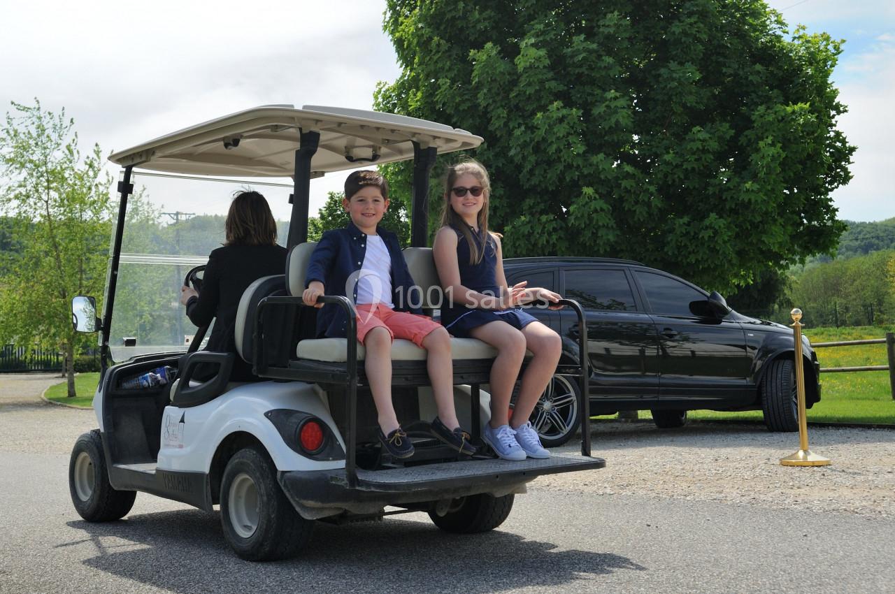 Deux enfants assis à l'arrière d'une voiturette de golf blanche, accompagnés d'un adulte conduisant.
