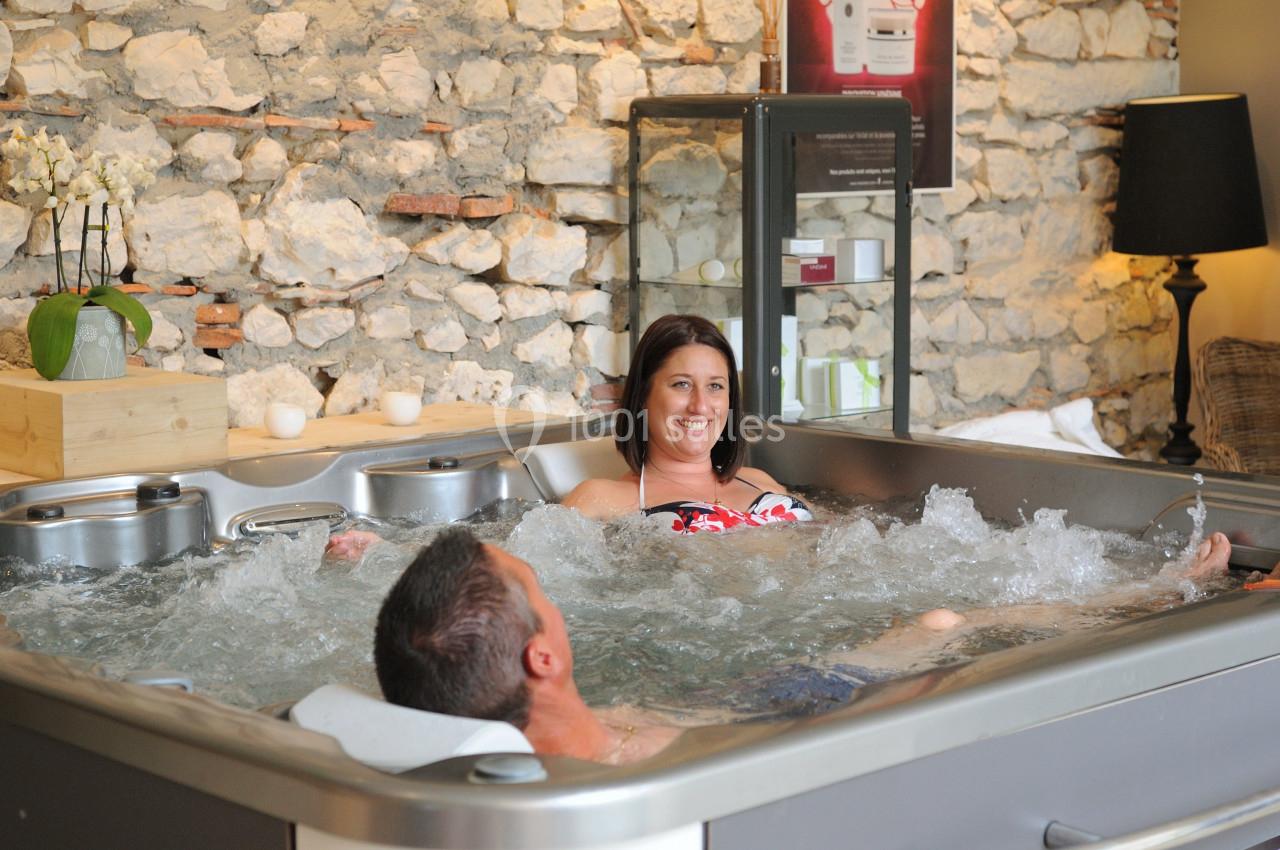 Deux personnes se détendent dans un jacuzzi intérieur, entouré de murs en pierre et d'une décoration chaleureuse.