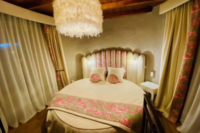 Chambre avec lit rond, couverture rouge, pétales de rose, lampe de chevet et plafond en bois avec suspension plumeuse.