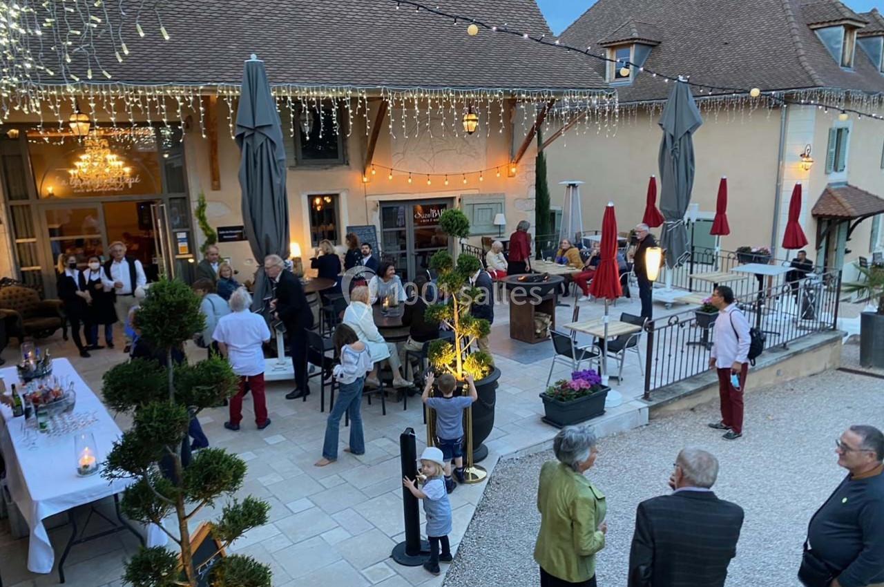 Groupe de personnes rassemblées dans une cour extérieure éclairée, avec tables, parasols et décorations lumineuses.
