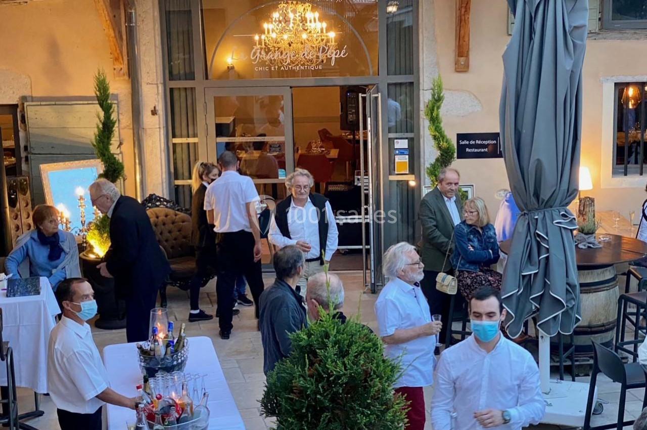 Groupe de personnes discutant dans une cour extérieure aménagée avec tables, plantes et éclairage décoratif.