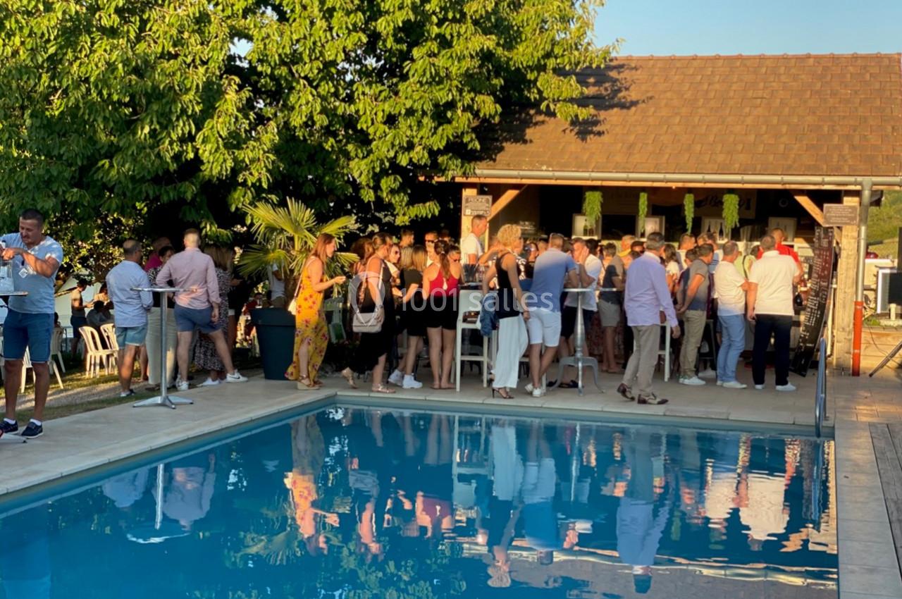 Groupe de personnes rassemblées près d'une piscine, devant un bar extérieur, sous un ciel dégagé en fin de journée.