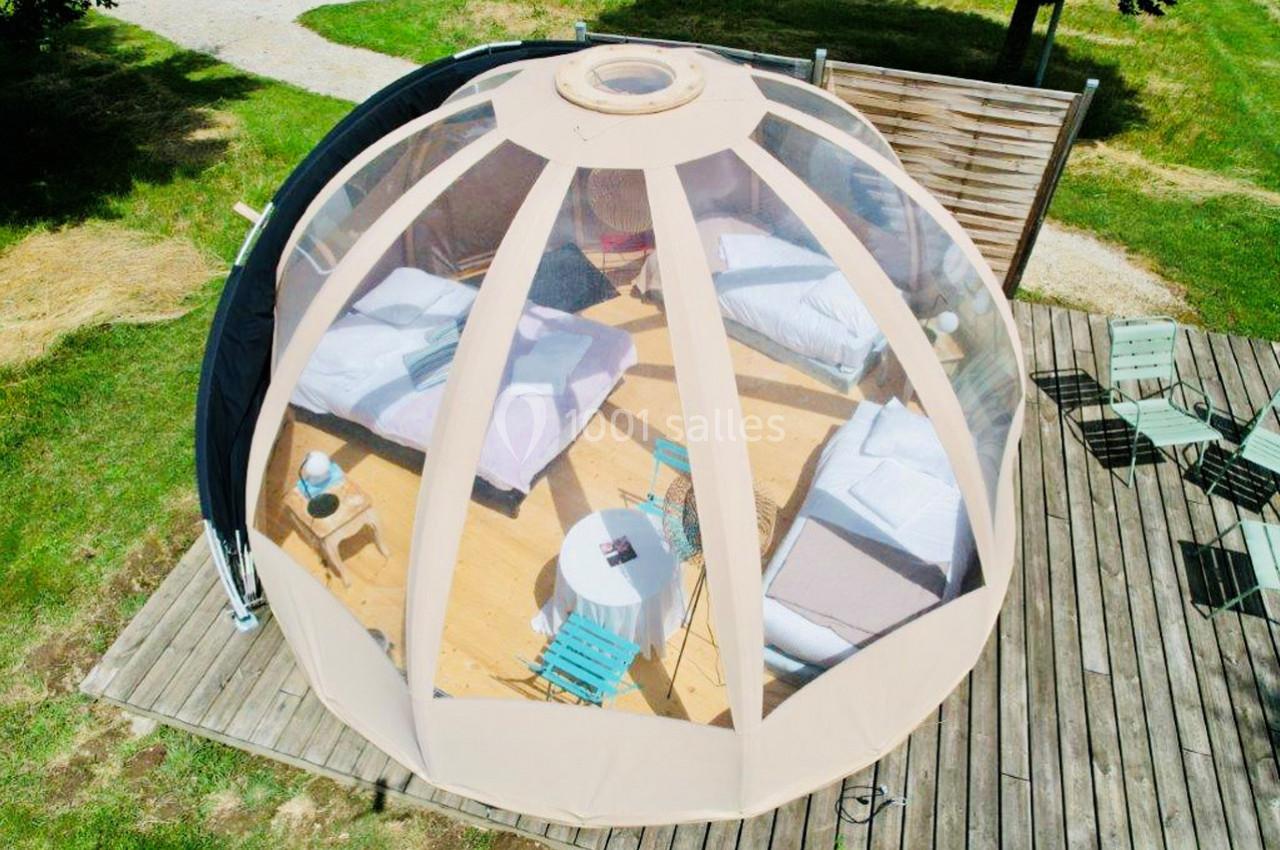 Vue aérienne d'une bulle transparente aménagée avec deux lits, une table et des chaises sur une terrasse en bois.