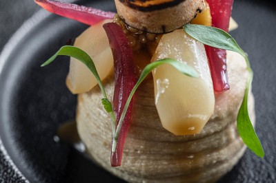 Chambre avec lit rond, couverture rouge, pétales de rose, lampe de chevet et plafond en bois avec suspension plumeuse.