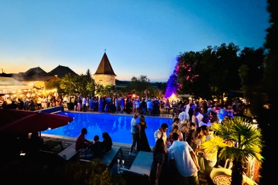 Chambre avec lit rond, couverture rouge, pétales de rose, lampe de chevet et plafond en bois avec suspension plumeuse.