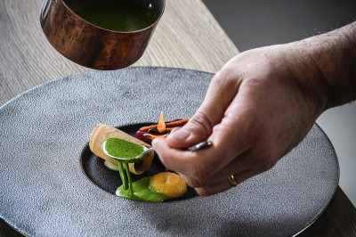 Chambre avec lit rond, couverture rouge, pétales de rose, lampe de chevet et plafond en bois avec suspension plumeuse.