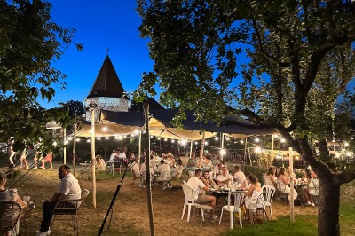 Chambre avec lit rond, couverture rouge, pétales de rose, lampe de chevet et plafond en bois avec suspension plumeuse.