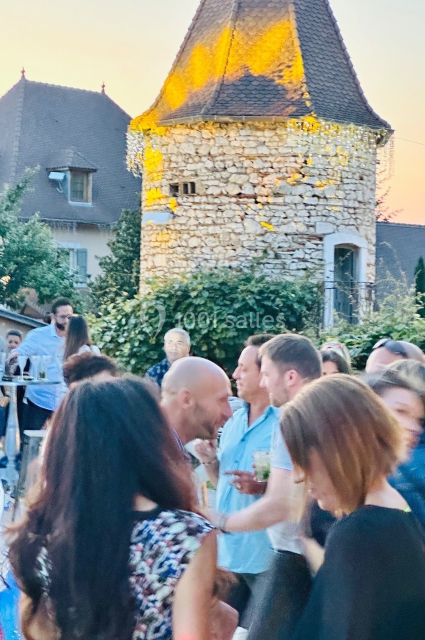 Groupe de personnes discutant lors d'un événement en plein air devant une tour en pierre au coucher du soleil.