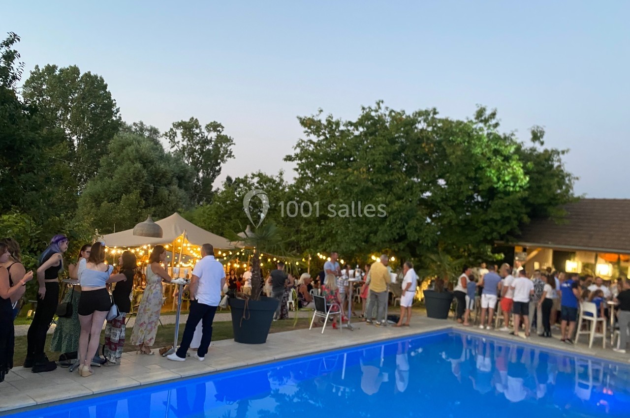 Groupe de personnes rassemblées près d'une piscine au crépuscule, avec guirlandes lumineuses et tentes dans un jardin.