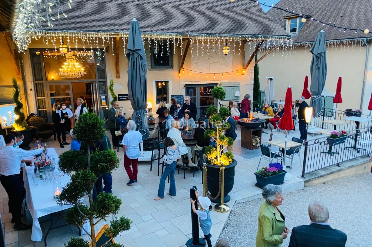 Groupe de personnes réunies dans une cour extérieure décorée de guirlandes lumineuses, en soirée.