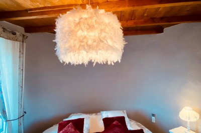 Chambre avec lit rond, couverture rouge, pétales de rose, lampe de chevet et plafond en bois avec suspension plumeuse.