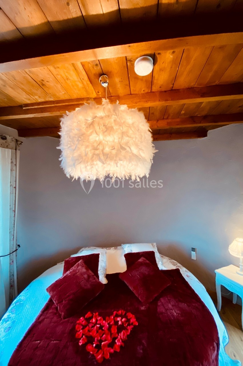 Chambre avec lit rond, couverture rouge, pétales de rose, lampe de chevet et plafond en bois avec suspension plumeuse.