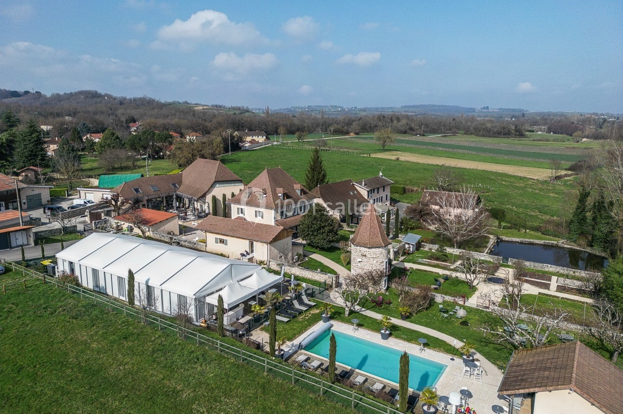 Vue aérienne d'un domaine avec piscine, bâtiments en pierre, chapiteau blanc et paysage rural environnant.