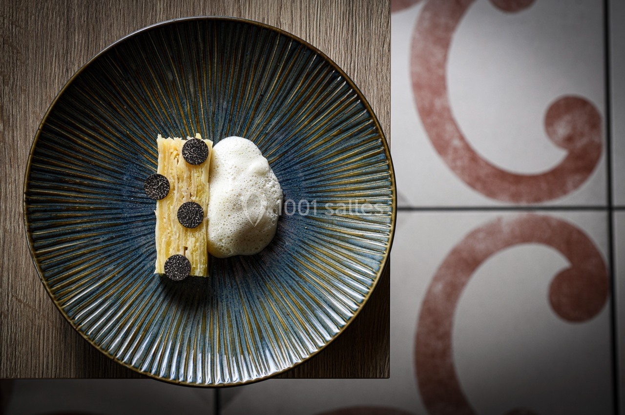 Assiette contenant un millefeuille de pommes de terre garni de truffes noires et accompagné d'une mousse légère.