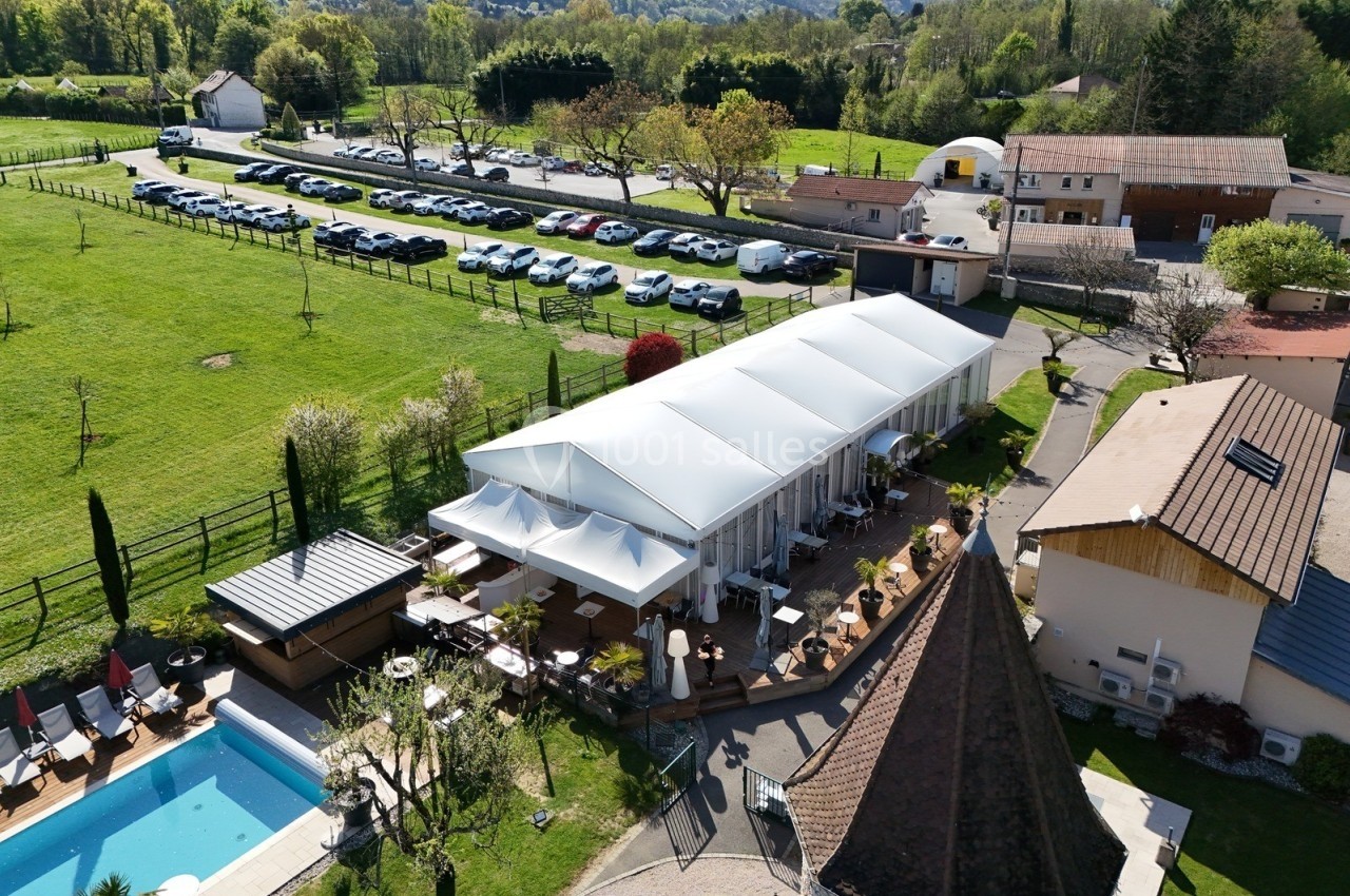 Vue aérienne d'une terrasse couverte entourée de verdure, avec une piscine et un parking à proximité.