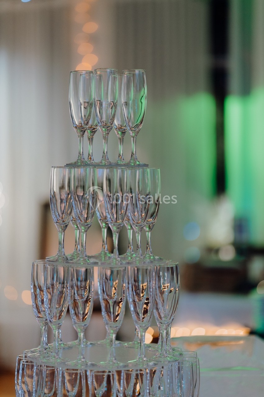 Pile de flûtes à champagne en verre disposées en pyramide dans un environnement lumineux et festif.