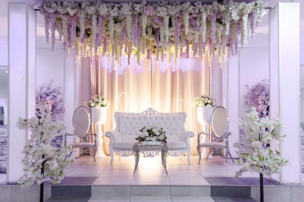 Décoration élégante avec canapé blanc, fleurs suspendues et arrangements floraux dans un espace lumineux.