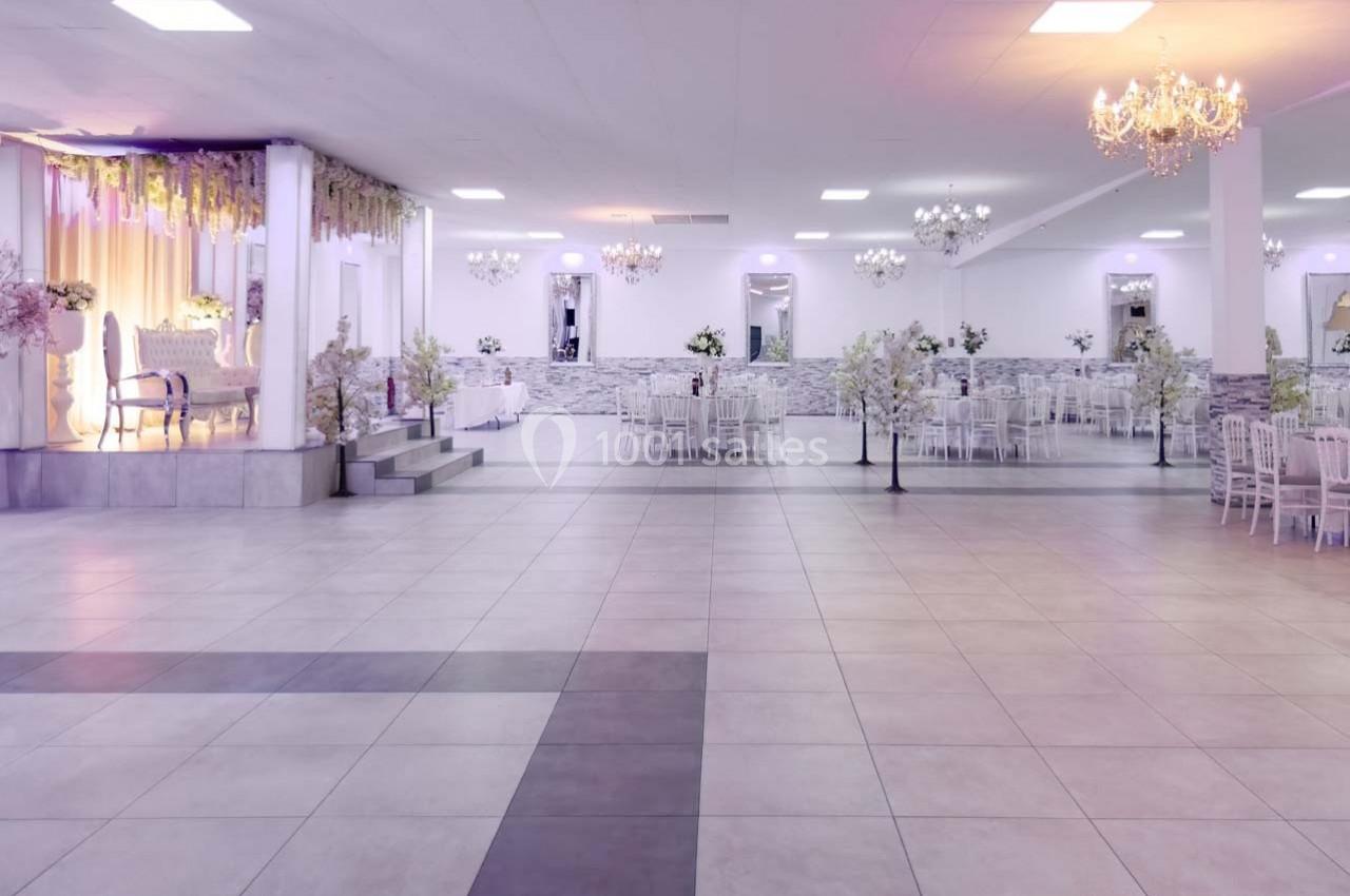 Salle de réception spacieuse avec tables décorées, lustres suspendus et éclairage doux.