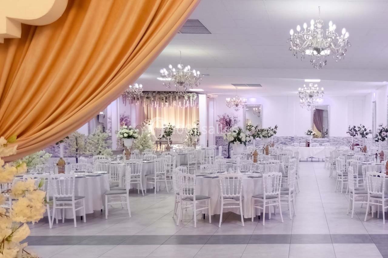 Salle de réception élégante avec tables rondes dressées, décorations florales et lustres suspendus.