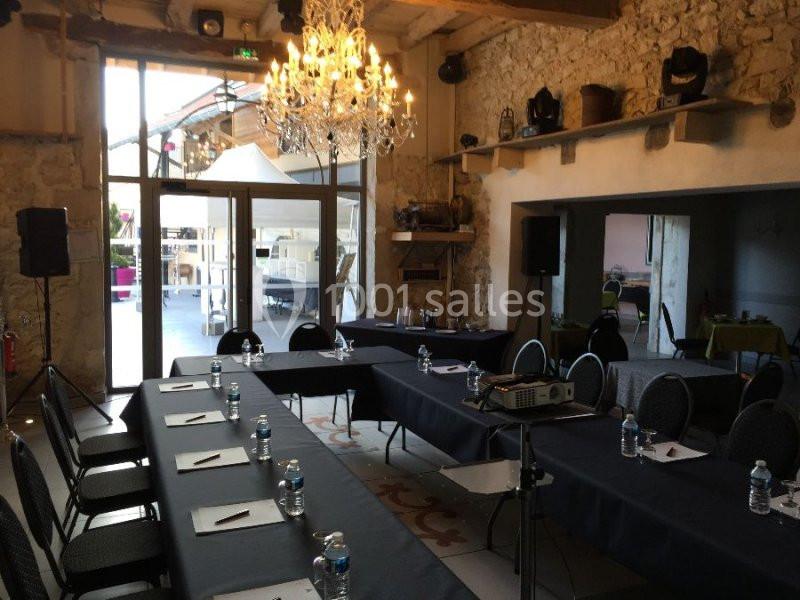 Salle de réunion lumineuse avec tables disposées en U, chaises, projecteur et vue sur une terrasse extérieure.