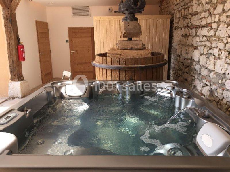 Bain à remous intérieur avec eau en mouvement, entouré de murs en pierre et de bois, dans un espace rustique.