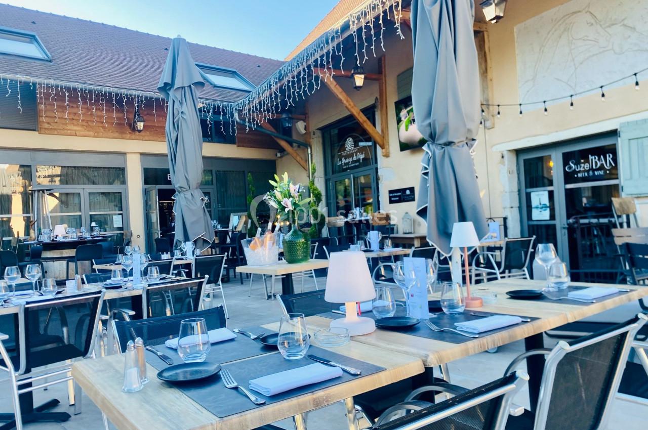 Terrasse d'un restaurant avec tables dressées, parasols gris, décoration florale et éclairage suspendu.