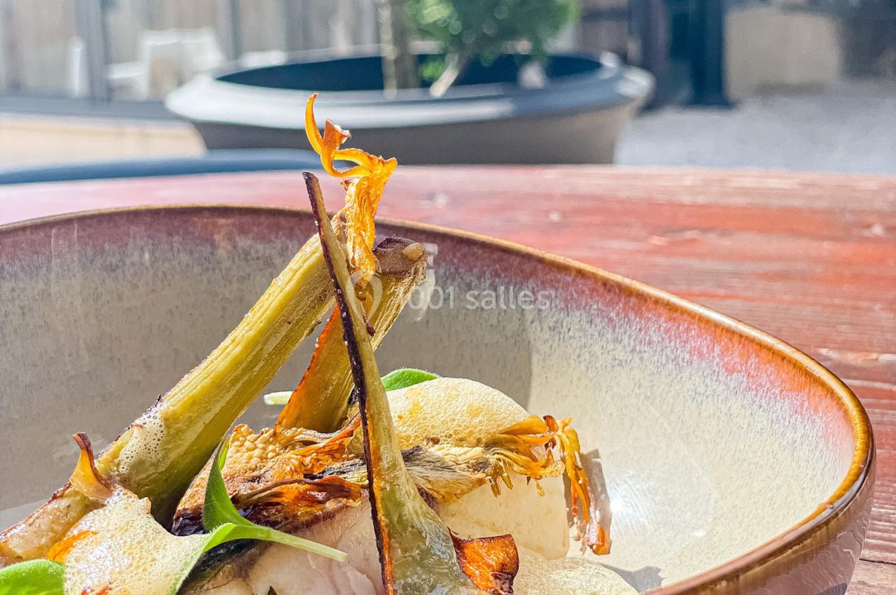 Assiette en céramique contenant un plat garni de légumes grillés, posée sur une table en bois en extérieur.
