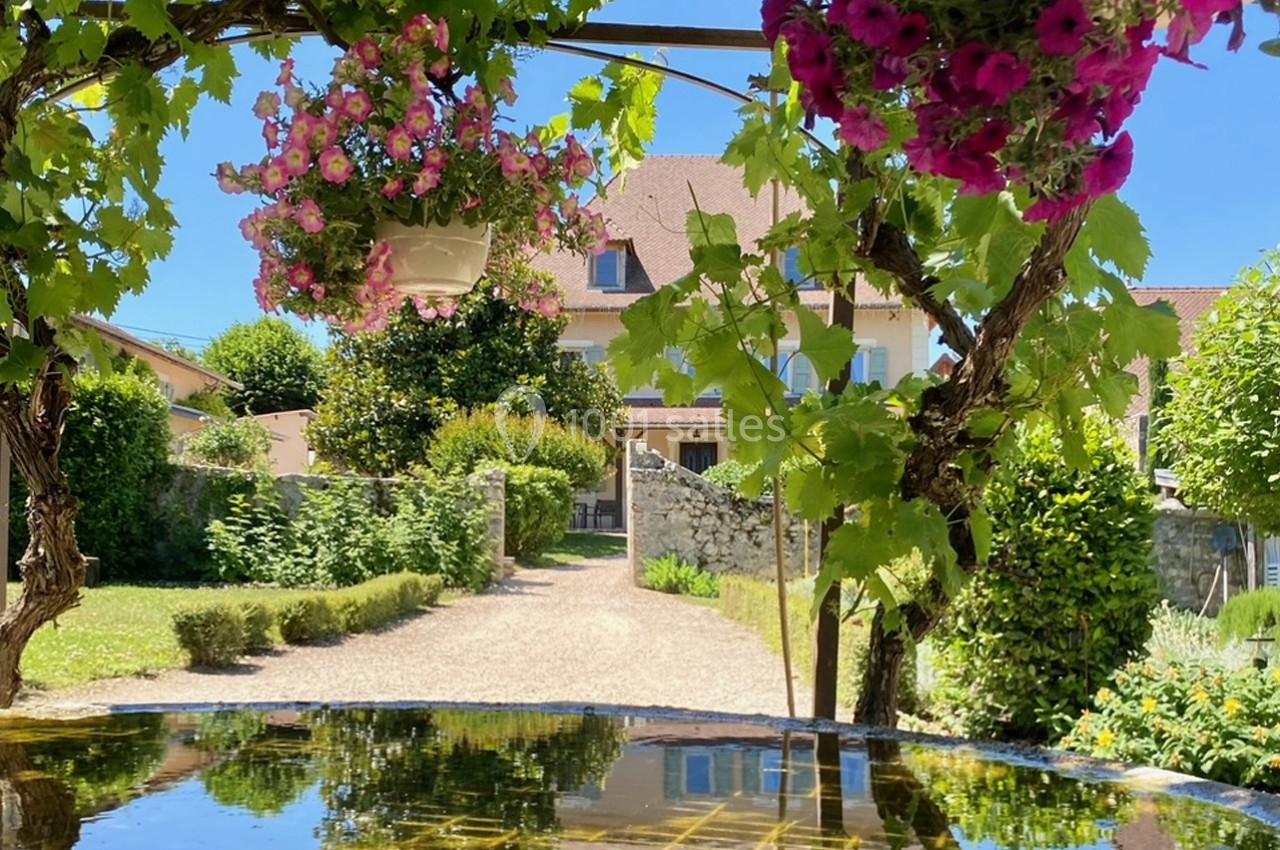 Allée de jardin bordée de verdure et de fleurs suspendues, menant à une maison avec un ciel dégagé en arrière-plan.