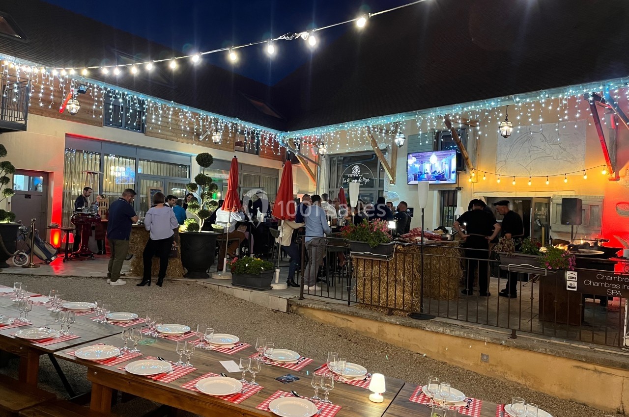 Cour extérieure éclairée en soirée avec des tables dressées, des invités debout et un buffet en arrière-plan.