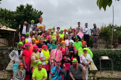 Vue aérienne d'un domaine rural avec des bâtiments, une tente beige, des espaces verts et des participants dispersés.