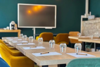 Vue aérienne d'un domaine rural avec des bâtiments, une tente beige, des espaces verts et des participants dispersés.