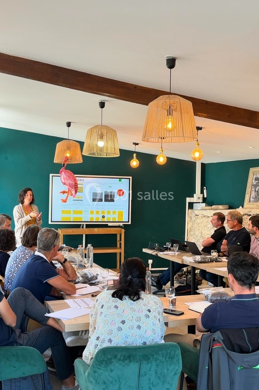 Une femme présente un diaporama sur un écran devant un groupe de personnes assises dans une salle lumineuse.