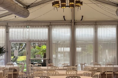 Vue aérienne d'un domaine rural avec des bâtiments, une tente beige, des espaces verts et des participants dispersés.