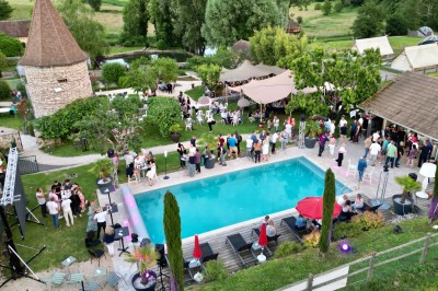 Vue aérienne d'une réception en plein air autour d'une piscine, avec des invités, des tables et des espaces verts…