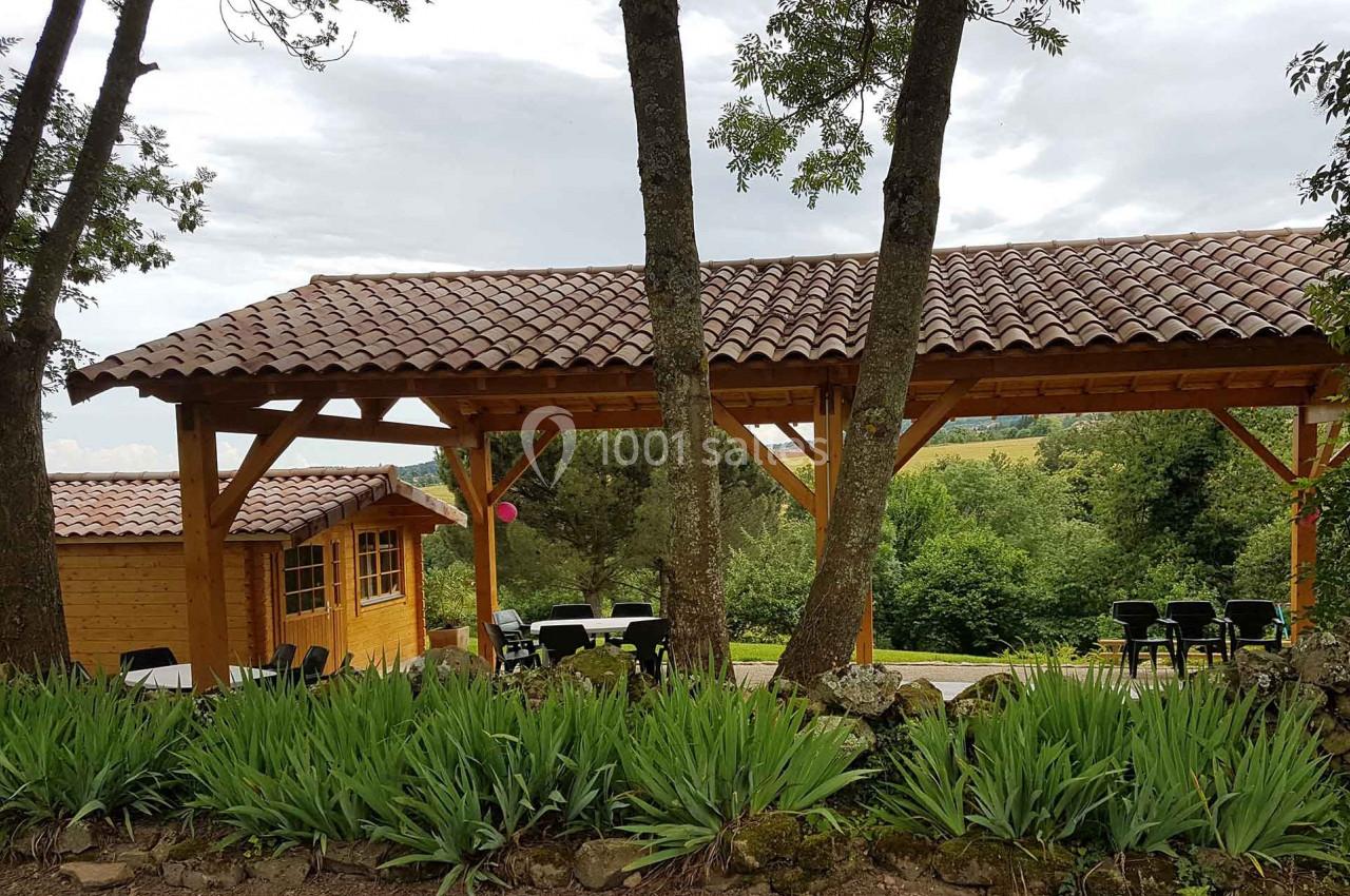 Abri en bois avec toit en tuiles, entouré d'arbres et de végétation, offrant une vue sur un paysage verdoyant.