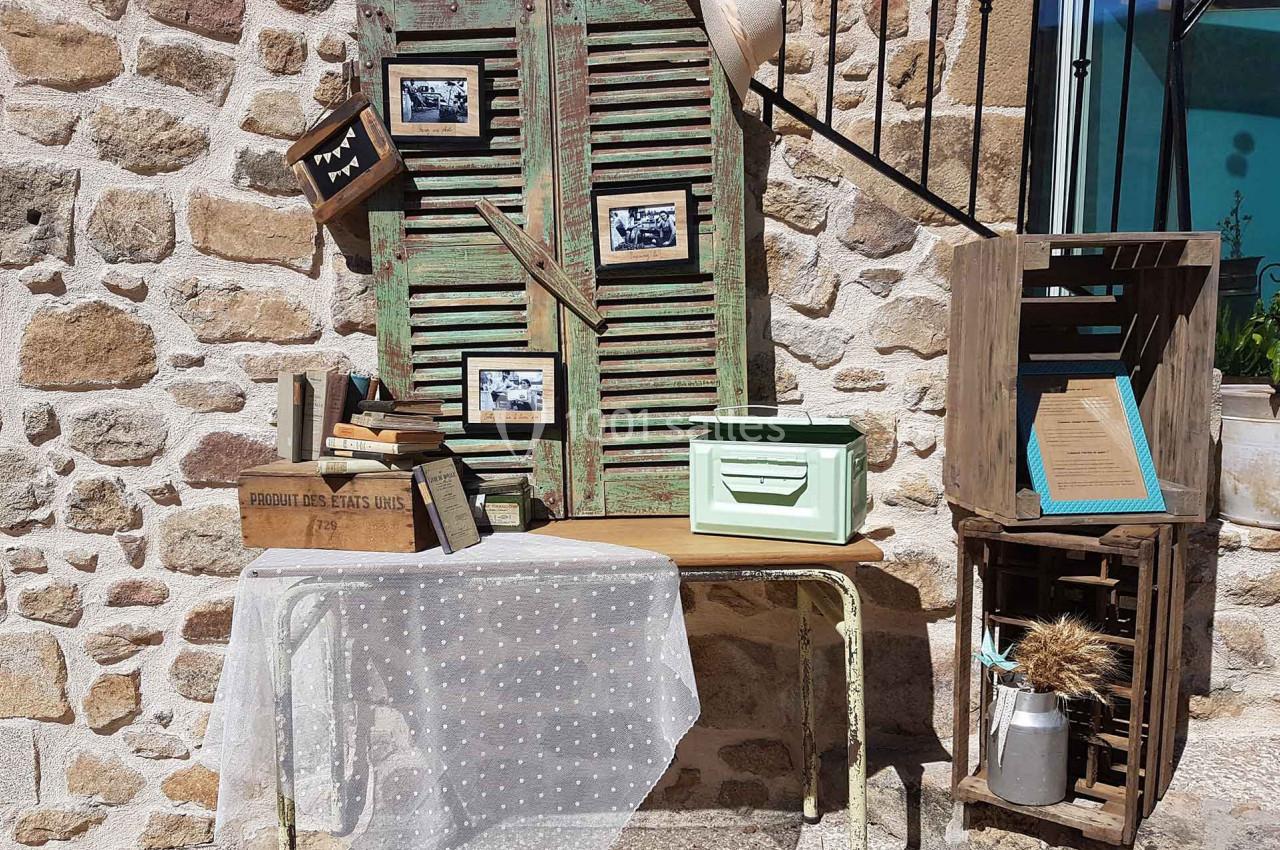 Décoration vintage avec volets en bois vieilli, cadres photo, livres anciens, caisse en métal et objets rétro sur une table.