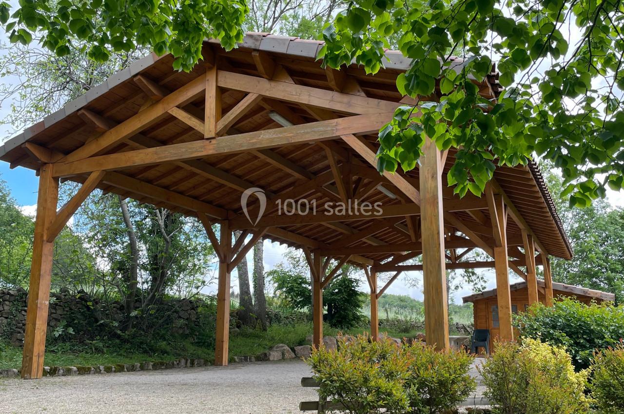 Abri en bois avec toit en tuiles, entouré de végétation et de pierres dans un cadre naturel.