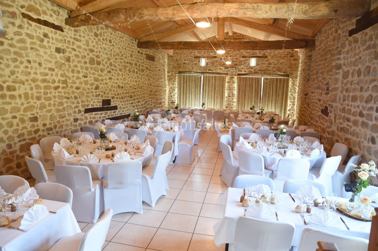Salle de réception en pierre avec tables rondes dressées, nappes blanches et décorations florales.