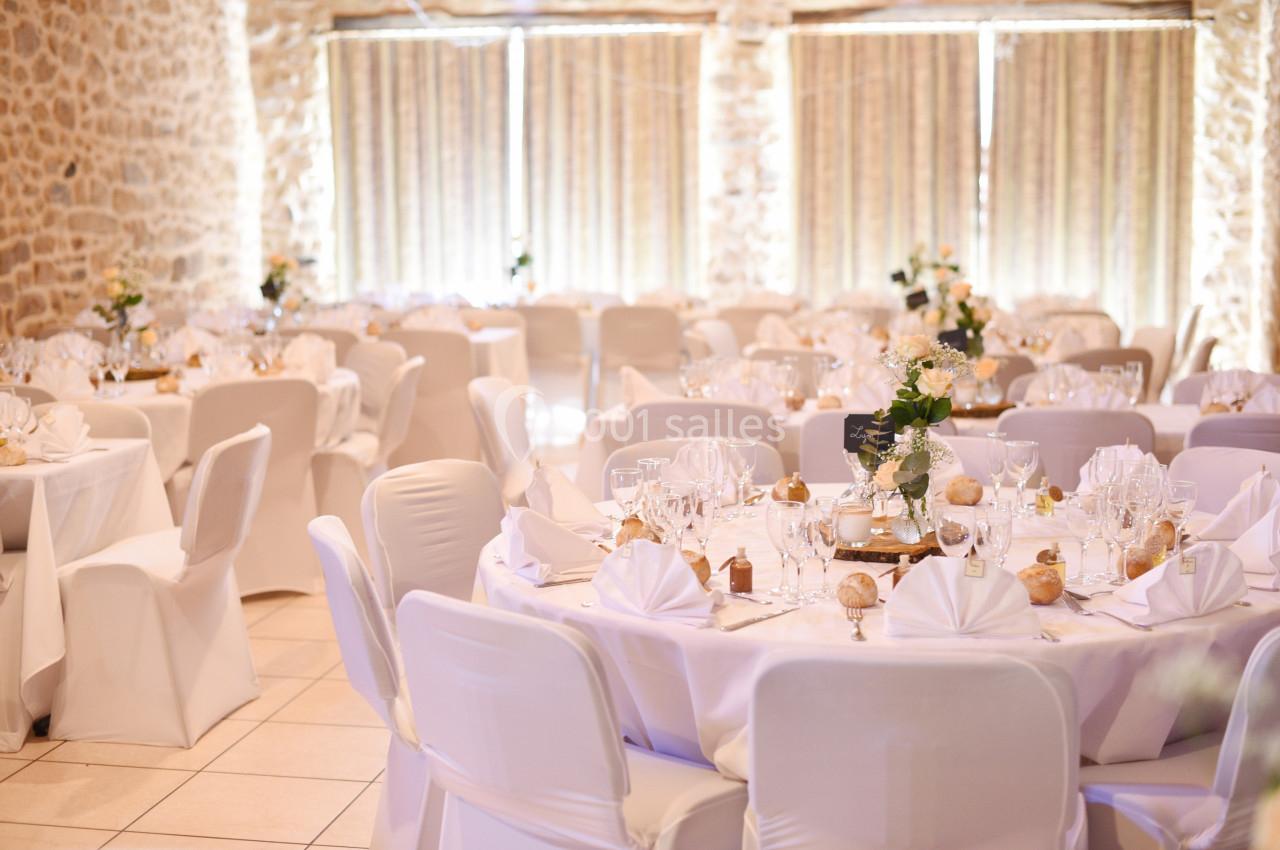 Salle de réception décorée avec des tables rondes, nappes blanches, vaisselle élégante et arrangements floraux.