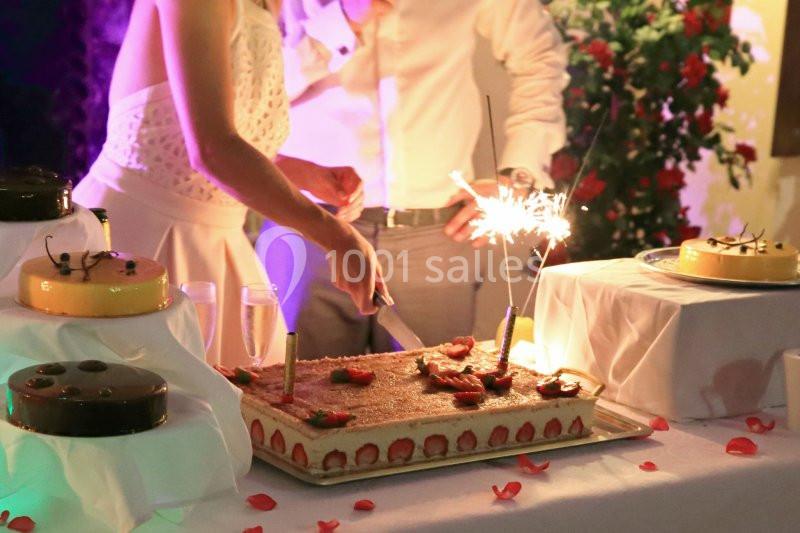 Une personne coupe un grand gâteau décoré de fraises et de bougies étincelantes lors d'une réception festive.