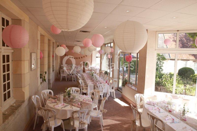 Salle de réception décorée avec des lanternes blanches et roses, tables rondes dressées pour un événement.