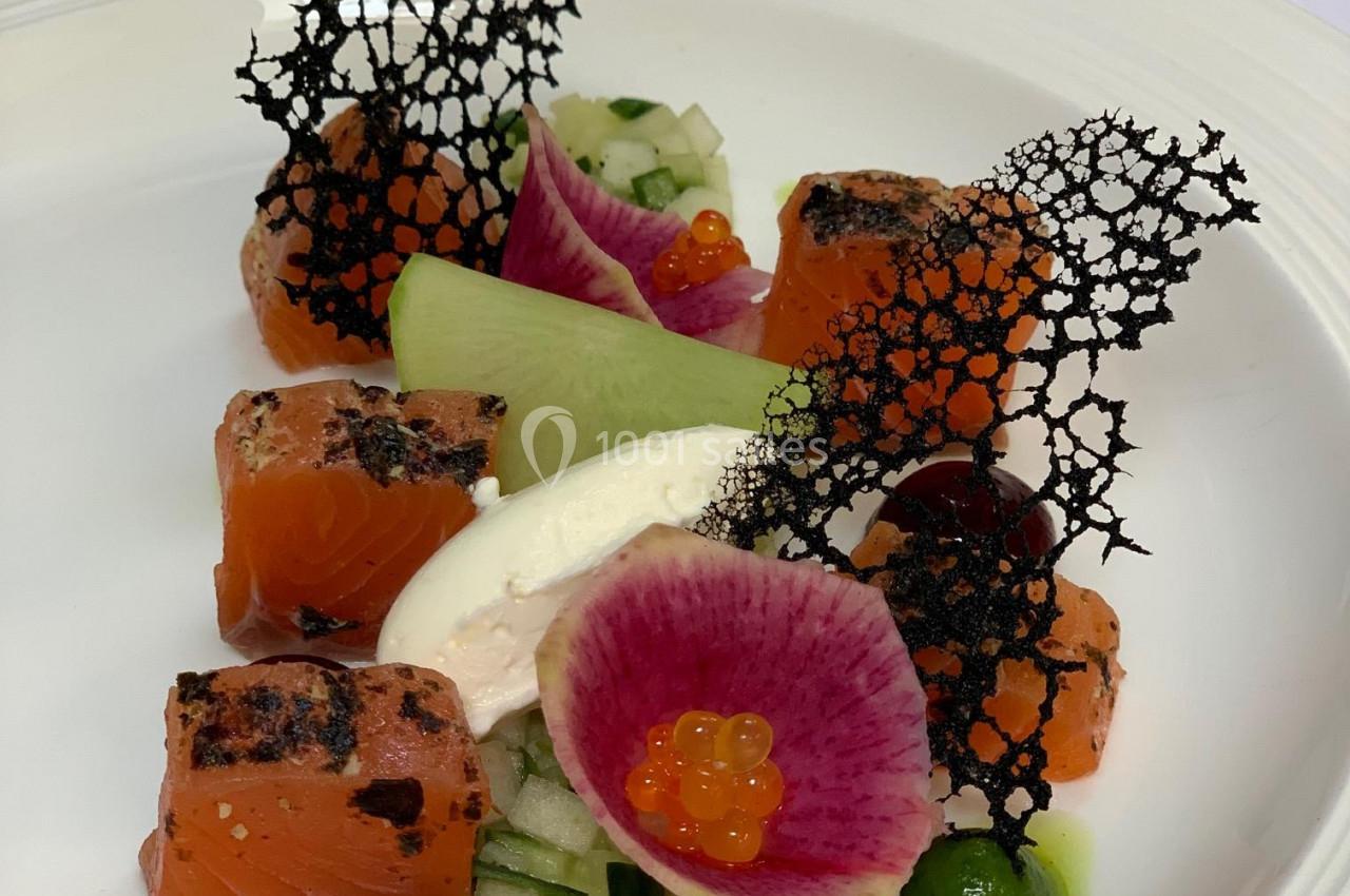 Assiette gastronomique avec saumon mariné, légumes croquants, crème, radis coloré, perles d'orange et décor noir ajouré.
