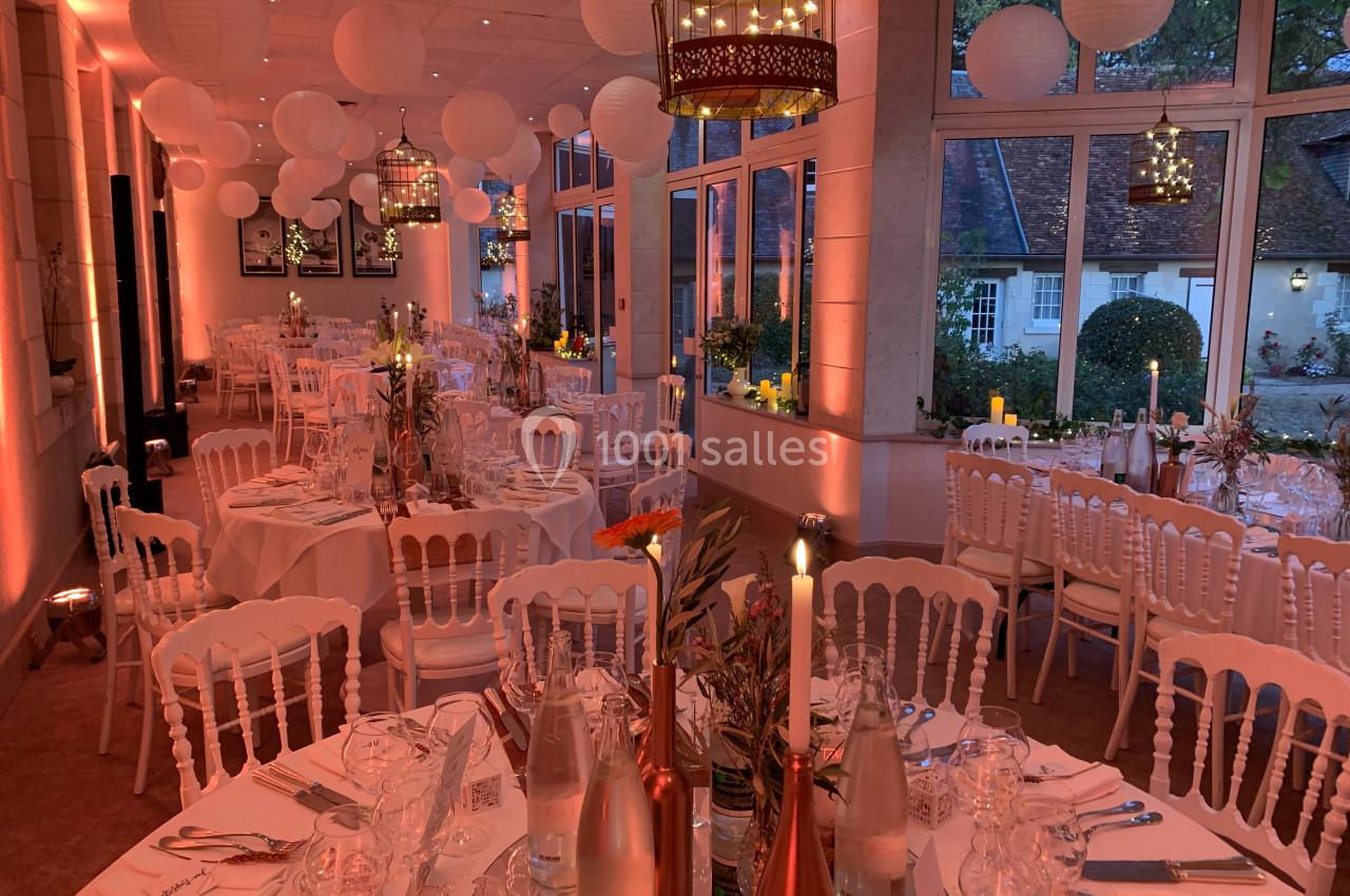 Salle de réception décorée avec des tables dressées, des lanternes suspendues et une lumière tamisée.