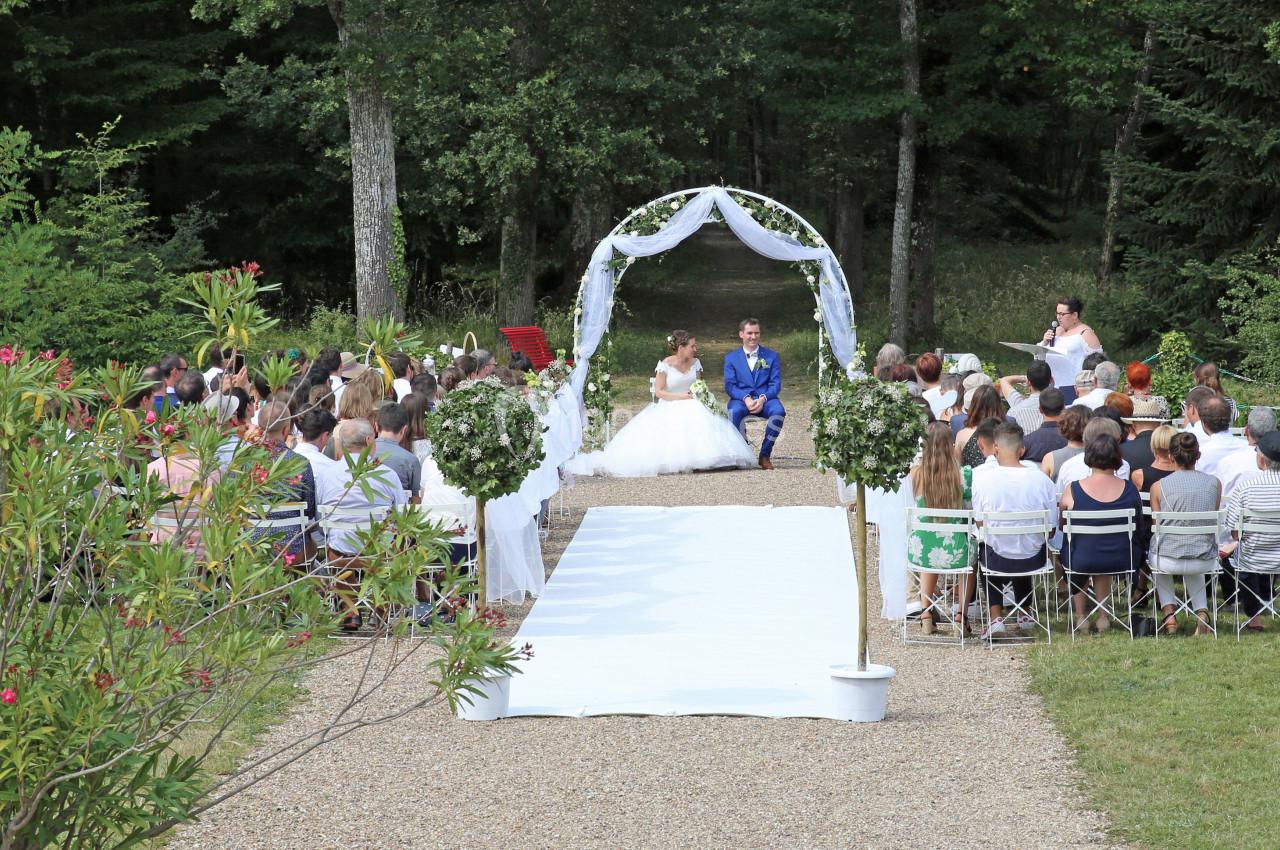 Cérémonie de mariage en plein air avec les mariés sous une arche blanche, entourés d'invités assis.