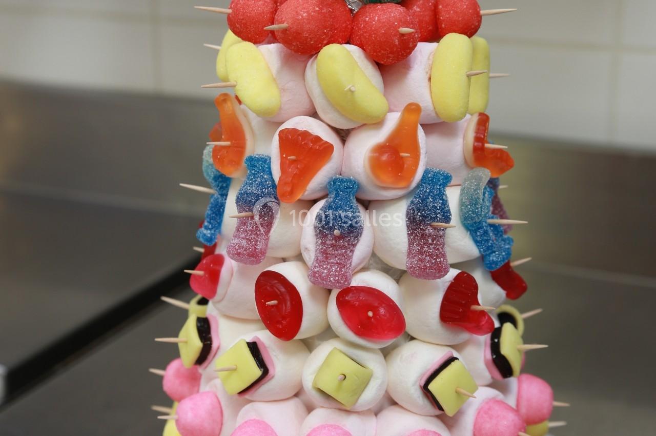 Tour de bonbons colorés composée de guimauves, sucettes et autres confiseries, montée sur une base circulaire.