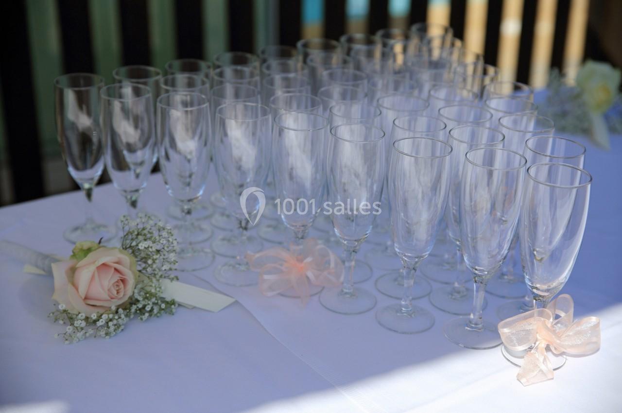 Rangée de flûtes à champagne vides sur une table blanche avec une rose et des rubans en décoration.