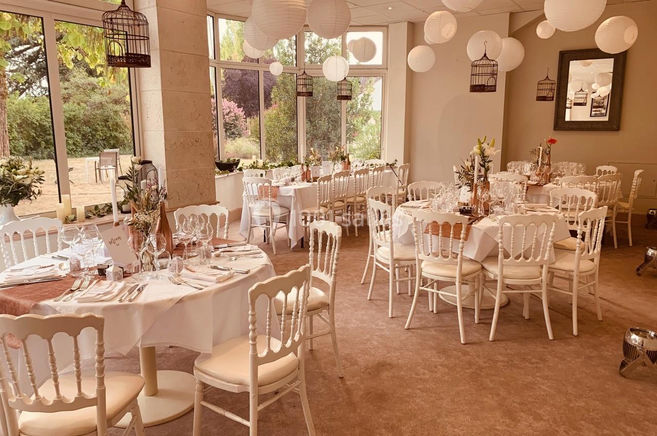 Salle de réception décorée avec des tables rondes dressées, des chaises blanches et des lanternes suspendues.