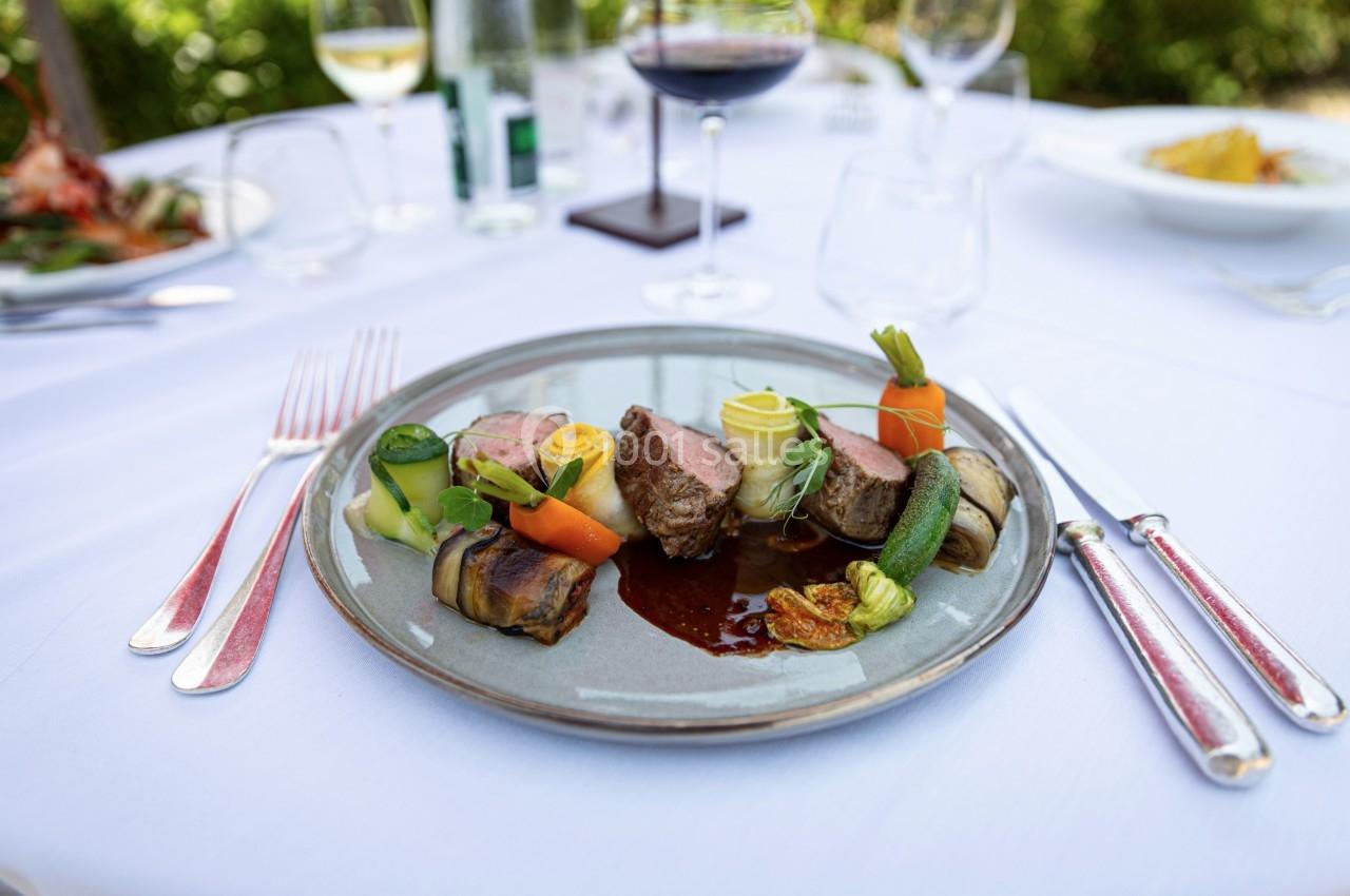 Assiette gastronomique avec viande, légumes variés et sauce, servie sur une table dressée en extérieur.