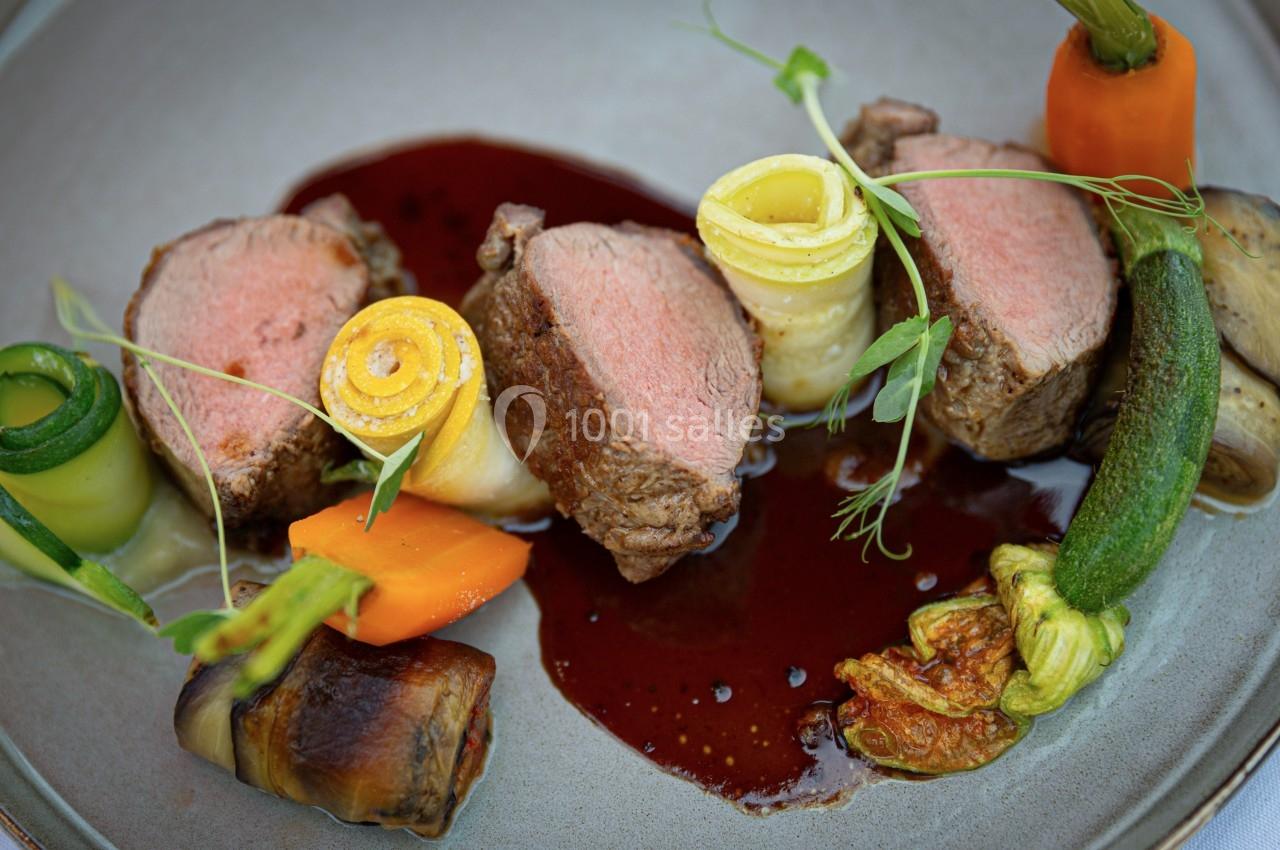 Assiette gastronomique avec morceaux de viande rosée, légumes colorés et sauce brune, présentée de manière raffinée.
